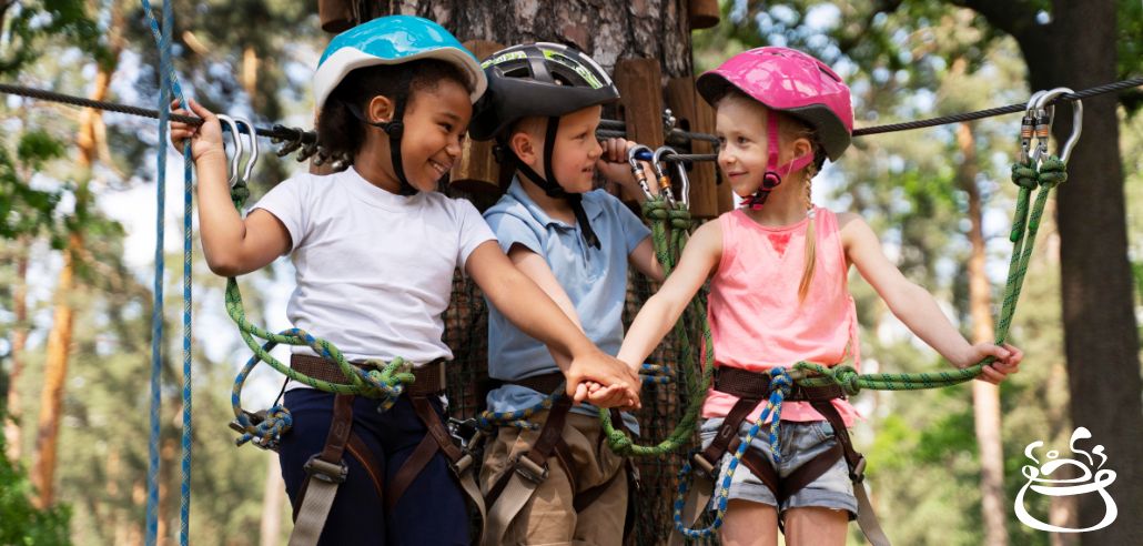 Kids in helmets and harnesses on a rope course, smiling