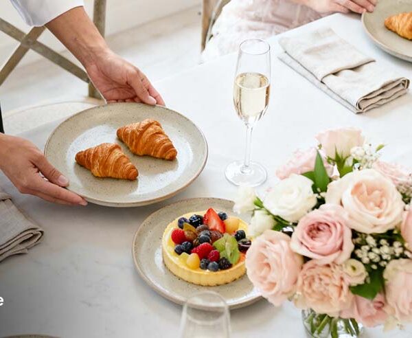 private chef serving croissants at an elegant bridal shower brunch table with fruit tarts, finger sandwiches, and flowers