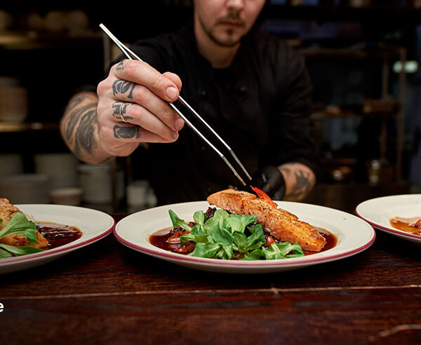 Personal chef plating seared salmon dishes with precision tweezers in a home kitchen