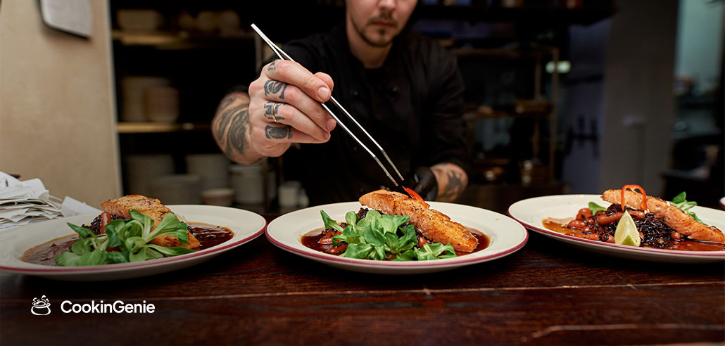 Personal chef plating seared salmon dishes with precision tweezers in a home kitchen